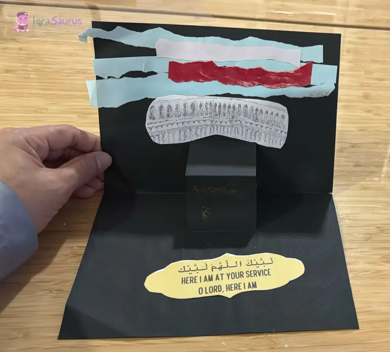 A pop-up Ka'bah on black card, with a torn-paper sky above it