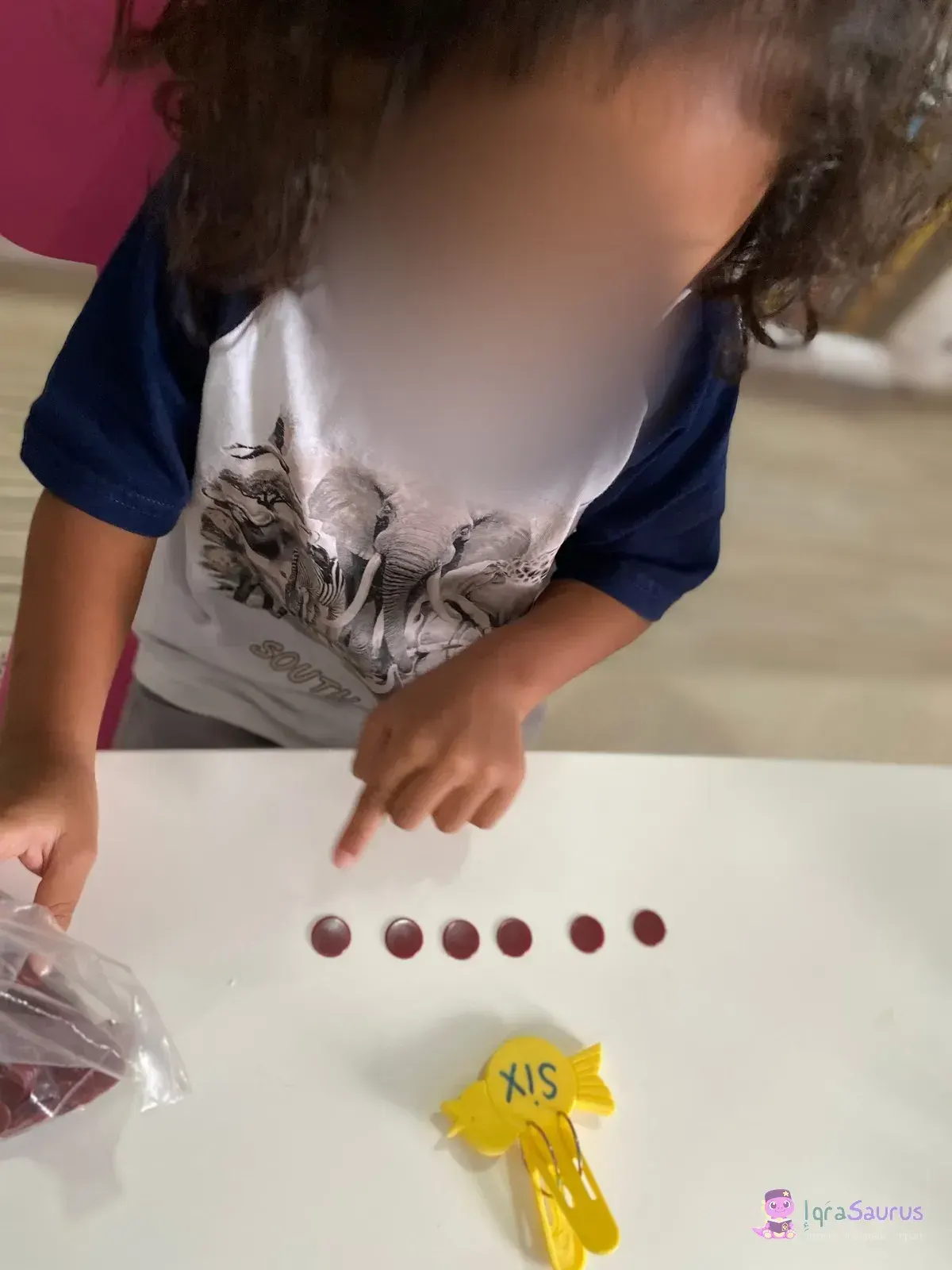 A child points along a row of six red counters beside the peg marked SIX