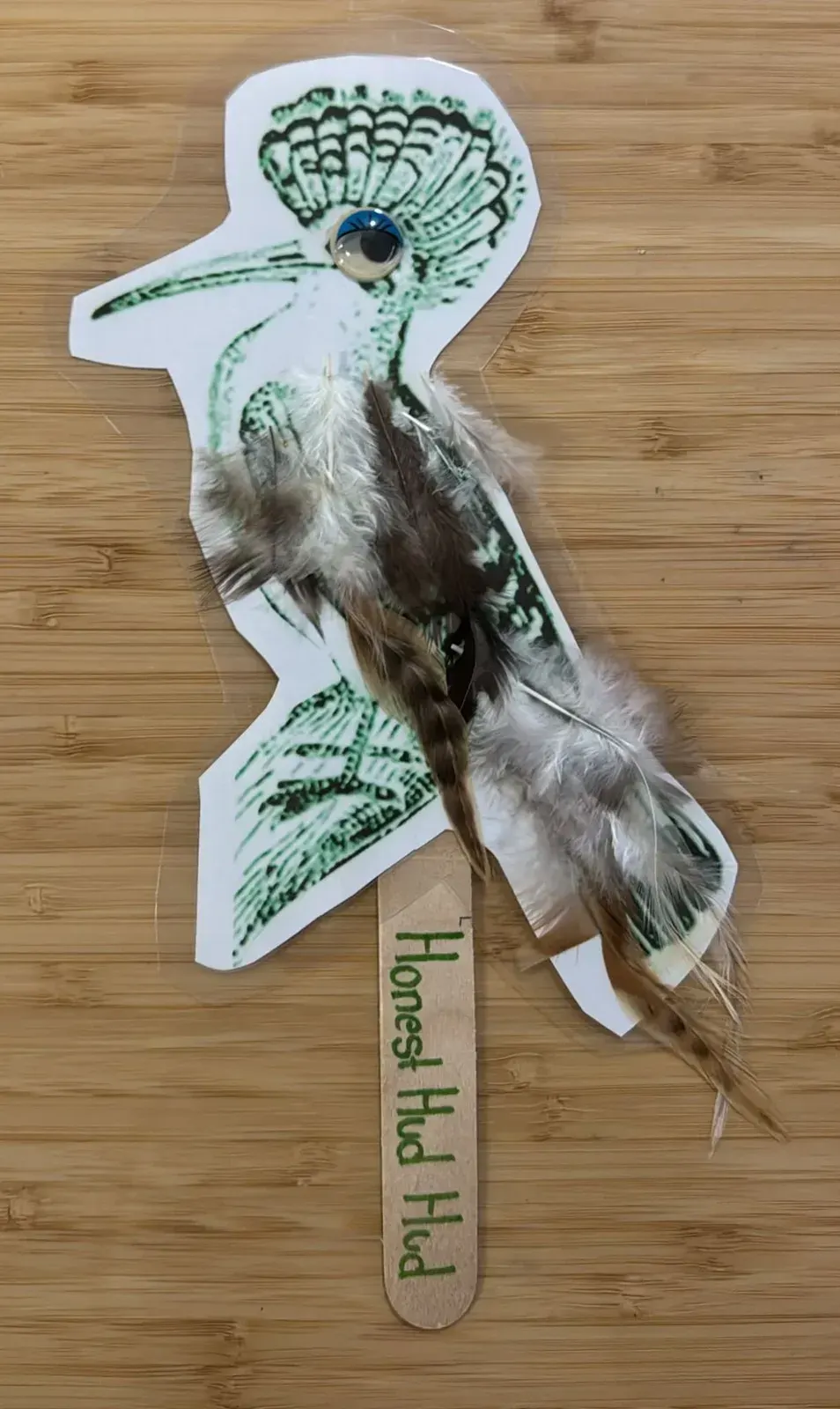 A hoopoe stick puppet with feathers, a googly eye and Honest Hudhud written on the stick